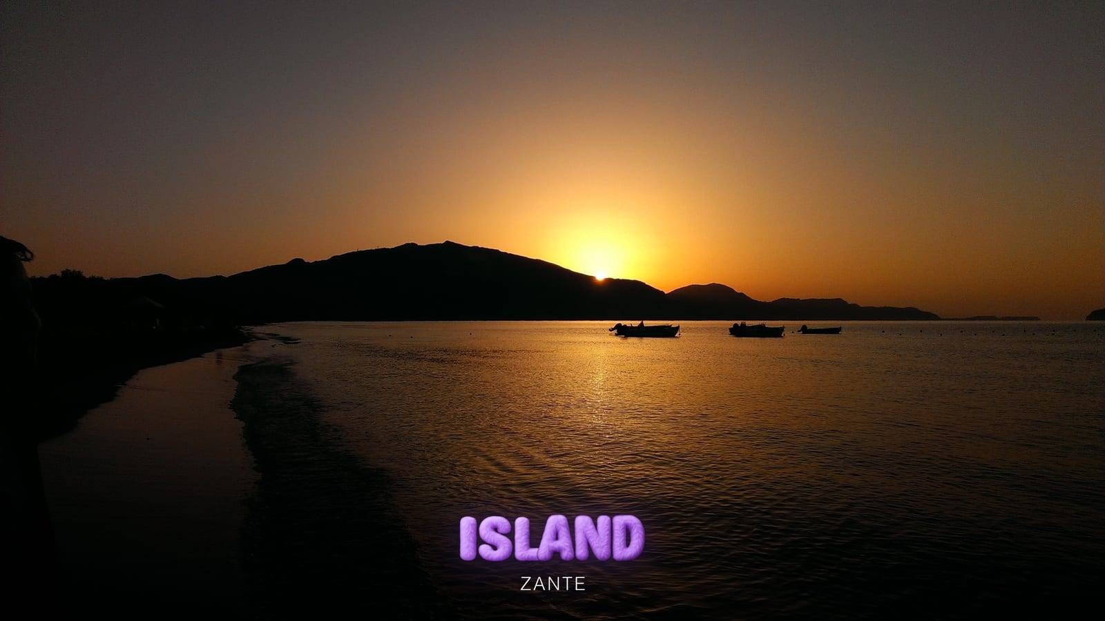 Sunset over the sea in Zante, the sun dropping behind the hills and boats in silhouette